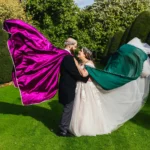 Couple with magenta and green capes flying in a topiary garden