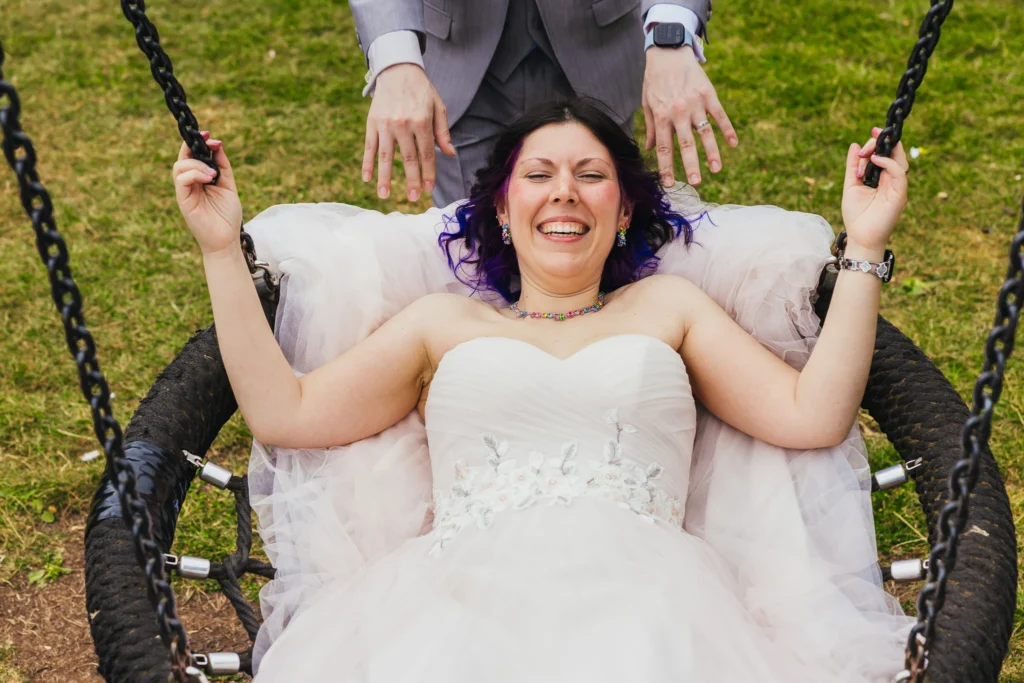 Laughing bride lying back on a rope swing as her partner pushes