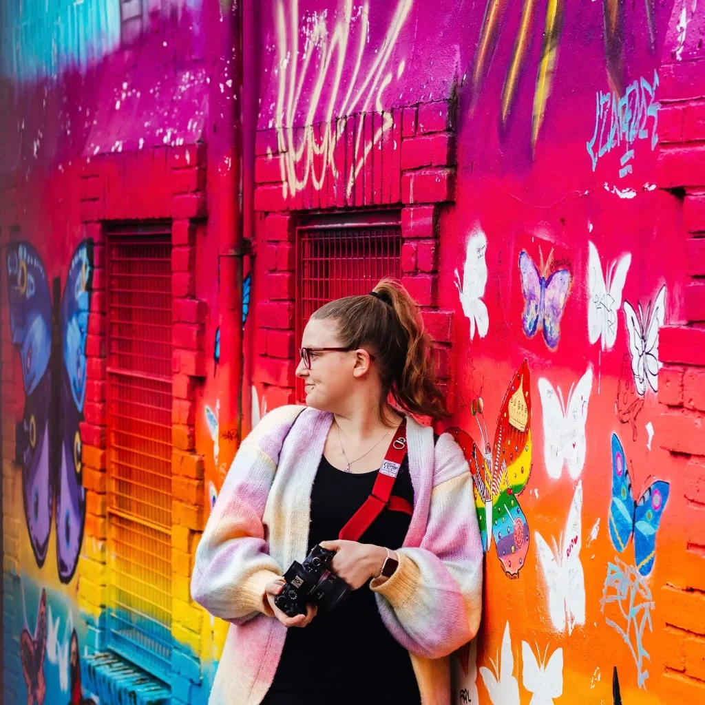 Kirsty Rockett holding her camera in front of a colourful butterfly mural