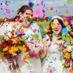 Two brides laughing under rainbow confetti