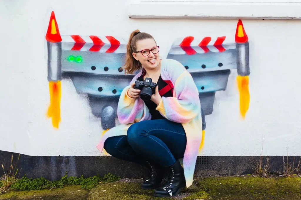 Kirsty crouching with her camera in front of a rocket mural