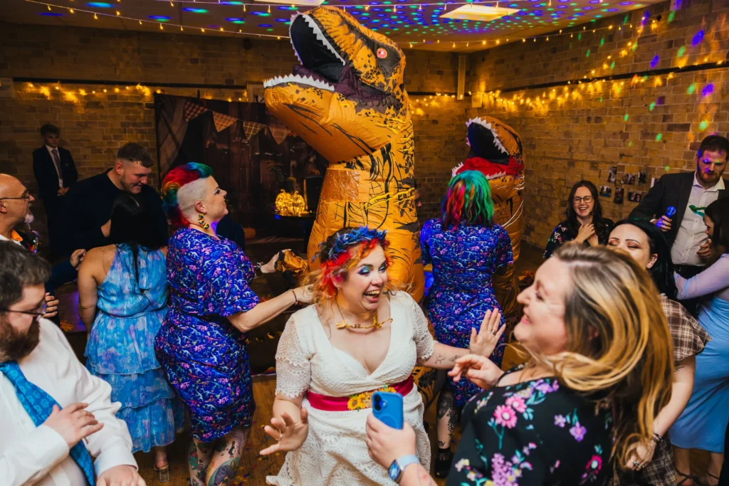 Bride with rainbow hair dancing with guests and inflatable dinosaurs
