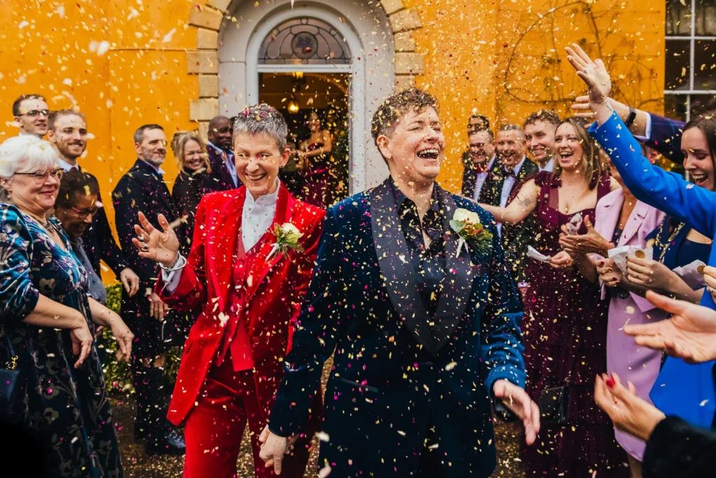 Couple in red and blue velvet suits in a confetti exit at Langar Hall