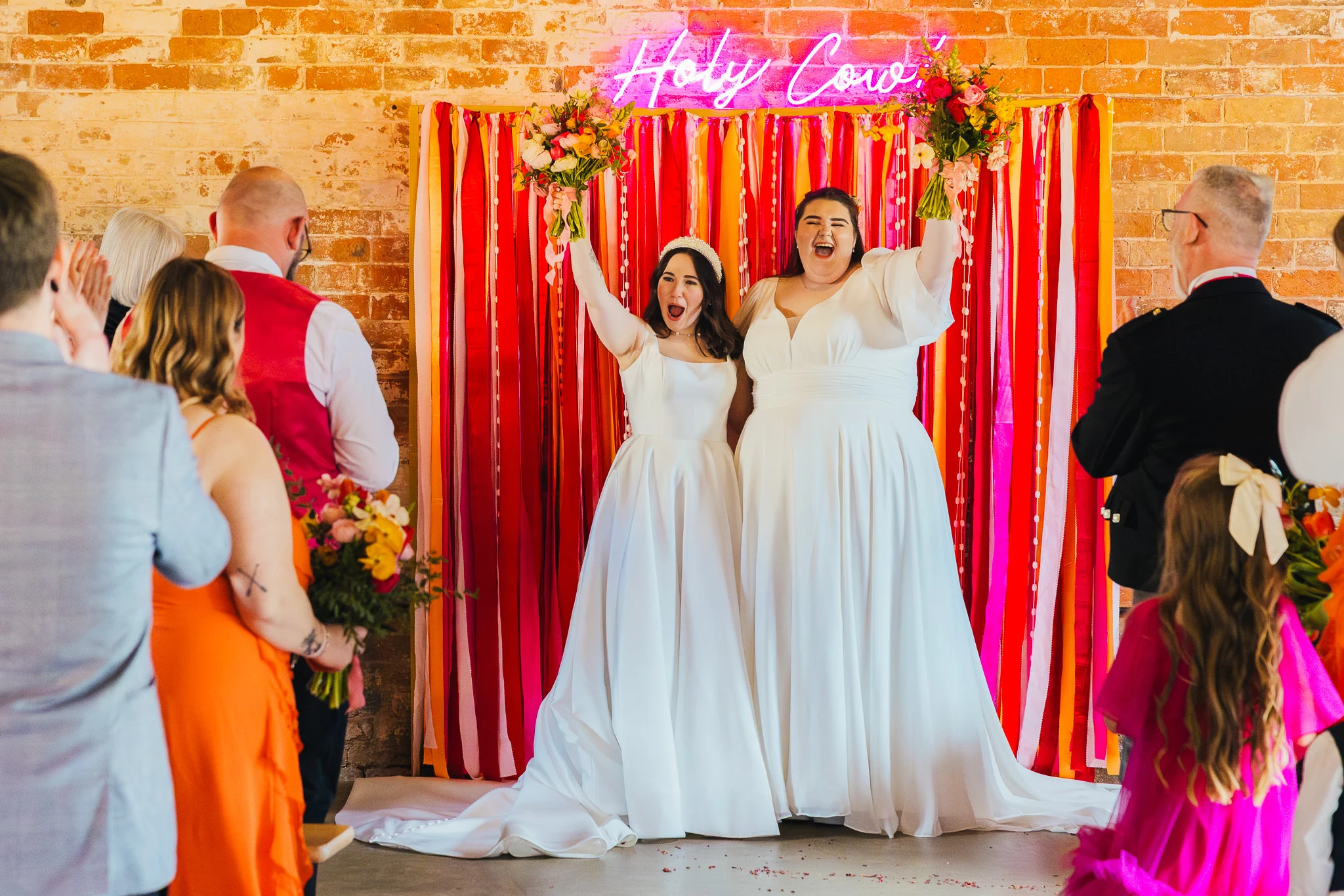 Two brides in front of a neon sign at The Old Cow Shed